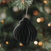 Schwarzer Papieranhänger in Kugelform am Weihnachtsbaum mit warm leuchtender Lichterkette