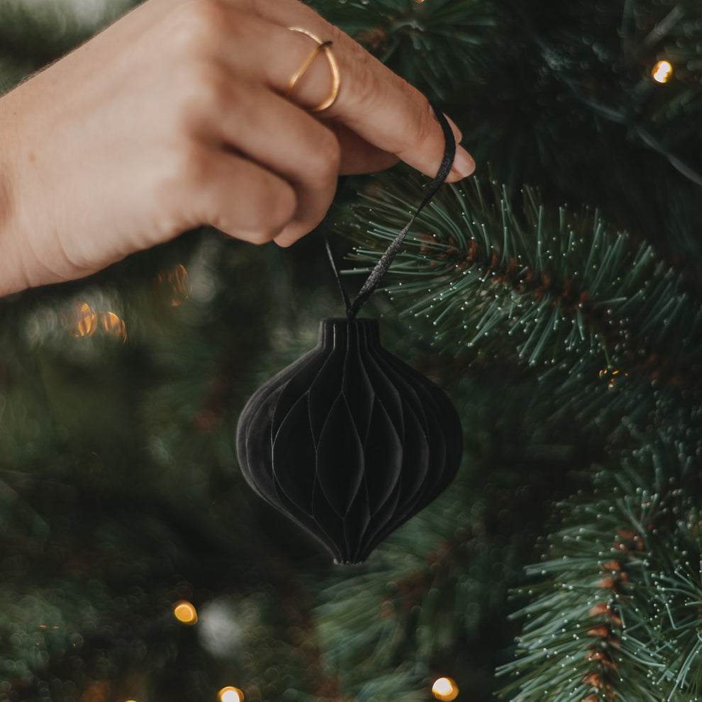 Schwarzer Papieranhänger in Kugelform wird als Christbaumschmuck am Weihnachtsbaum aufgehängt