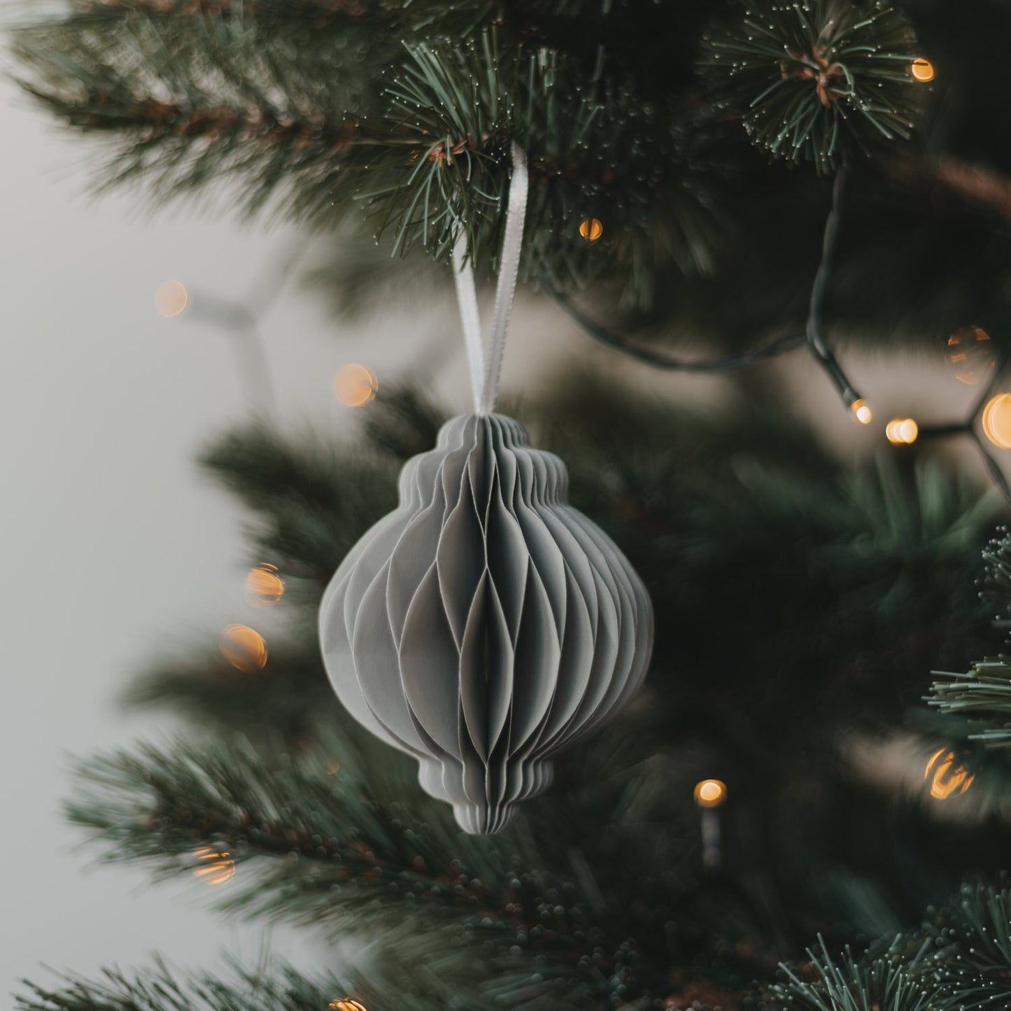 Grauer Papieranhänger in Kugelform am Weihnachtsbaum mit warmen Lichtern