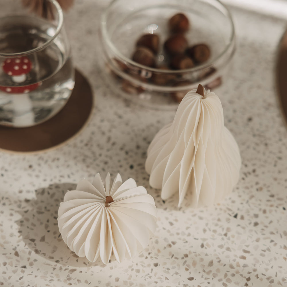 Zwei kleine weiße Papierkürbisse mit feiner Faltstruktur als minimalistische Herbstdeko