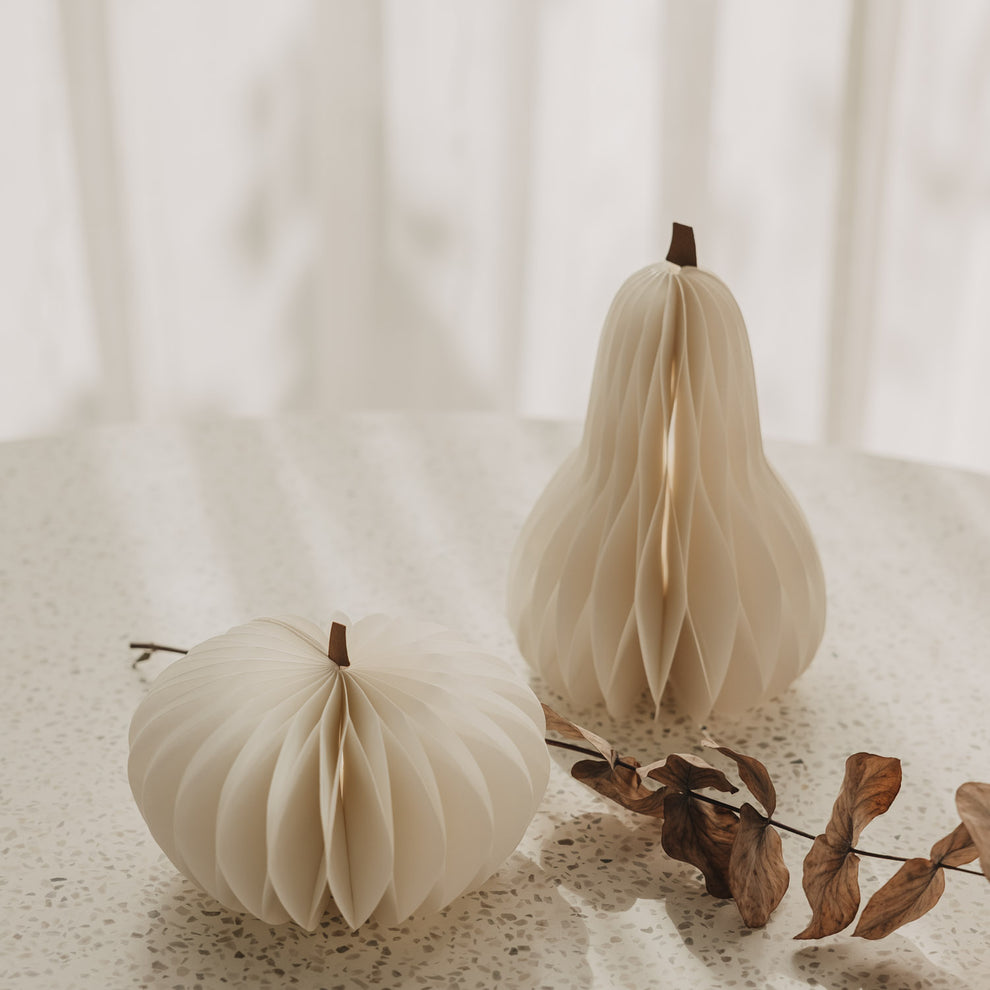 Zwei große weiße Papierkürbisse mit Wabenstruktur und getrocknetem Zweig als minimalistische Herbstdeko