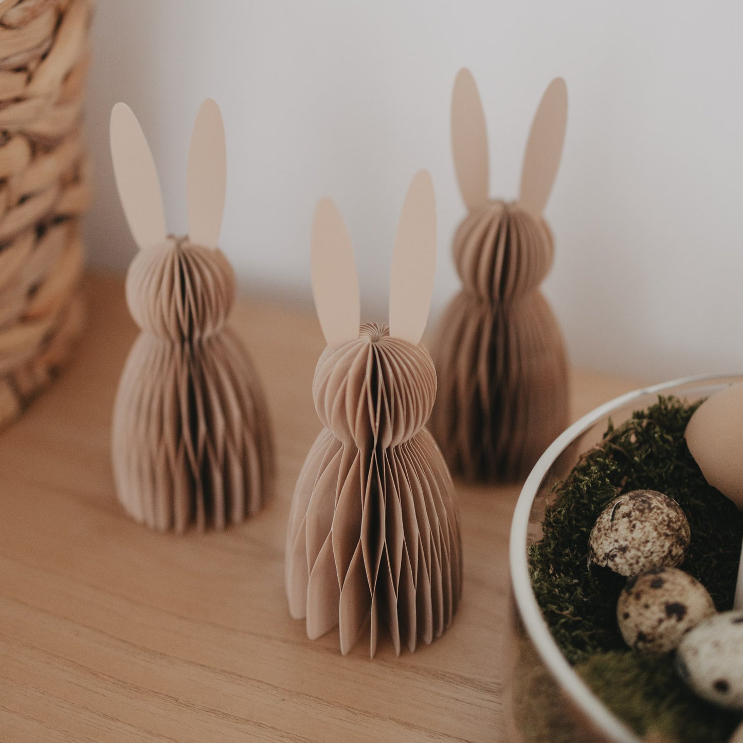 Drei naturfarbene Papierhasen als Dekofiguren auf Holzoberfläche mit feiner Wabenstruktur.