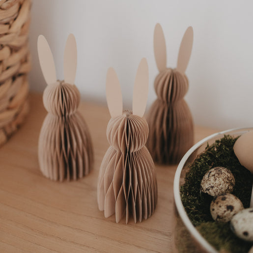 Drei naturfarbene Papierhasen als Dekofiguren auf Holzoberfläche mit feiner Wabenstruktur.