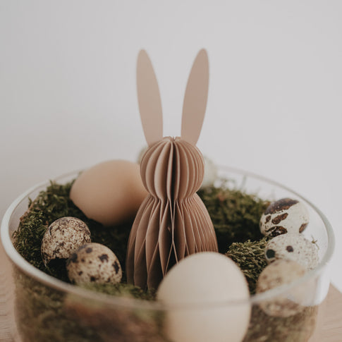 Naturfarbener Papierhase in Wabenoptik als Osterdeko zwischen Moos und Eiern in einer Glasschale.