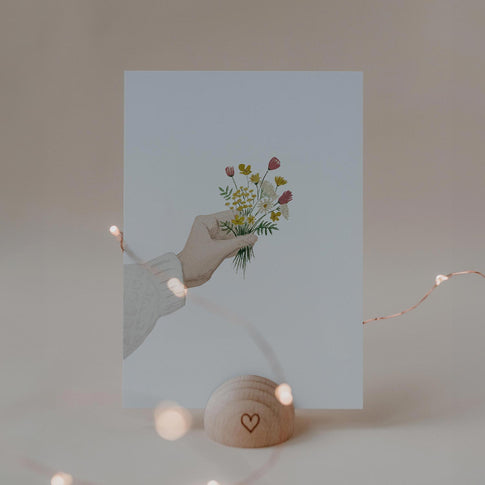 Eulenschnitt Aquarellkarte mit einer Hand, die einen bunten Wiesenblumenstrauß hält, im Kartenhalter aus Holz.