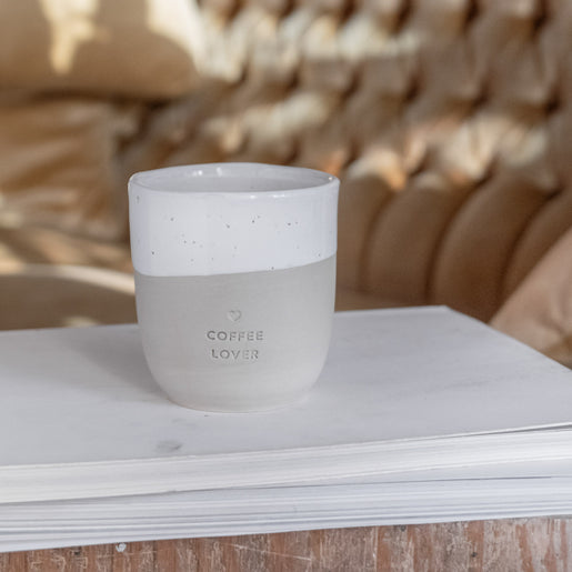 Ein Becher mit der Prägung "Coffee Lover" steht auf einem Tisch vor einem Sofa.