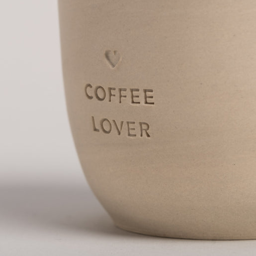 Nahaufname von einem Becher mit der Prägung "Coffee Lover" im Fokus.