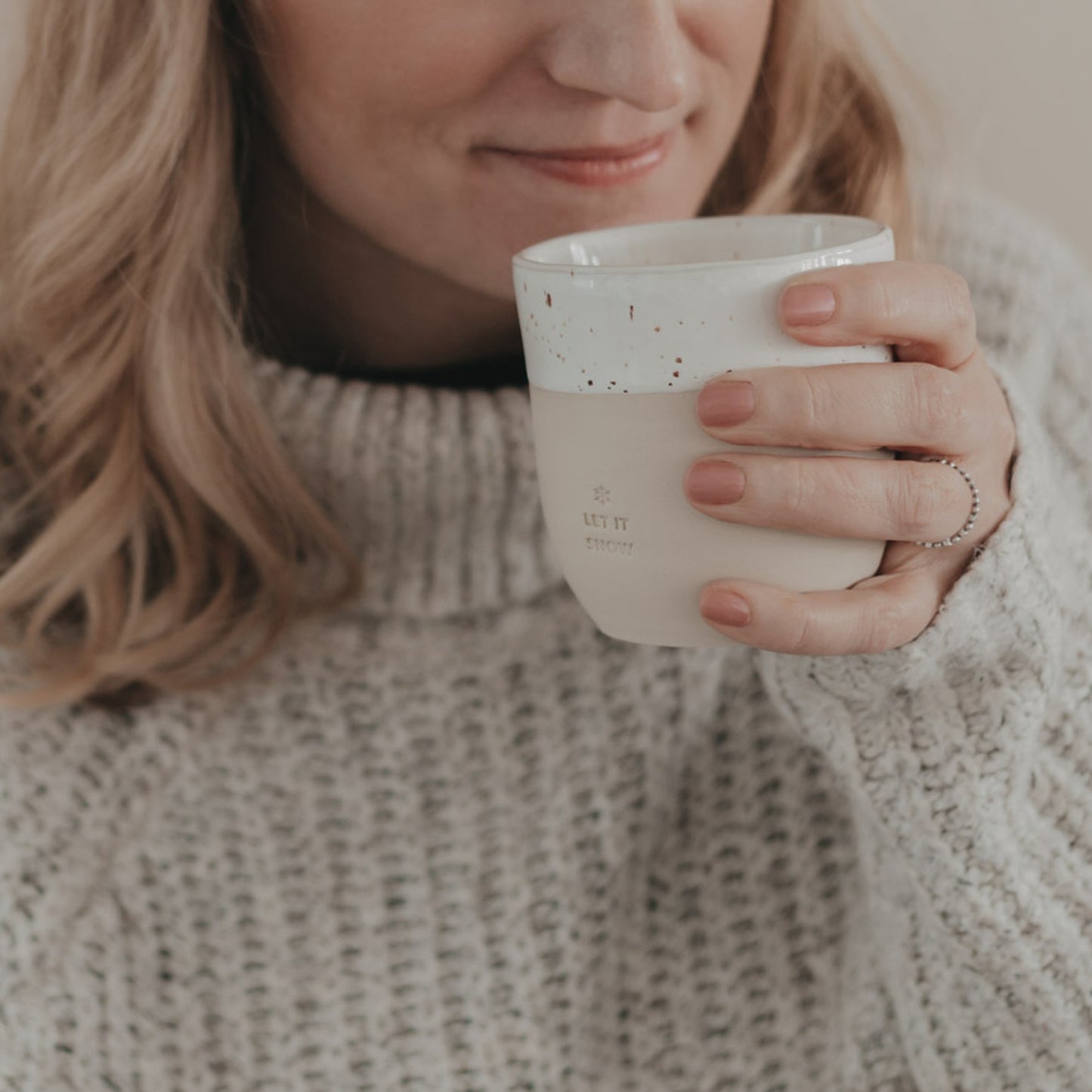 Frau in Strickpullover genießt ein Getränk aus dem handgefertigten Steingutbecher „Let it Snow“ von Eulenschnitt.