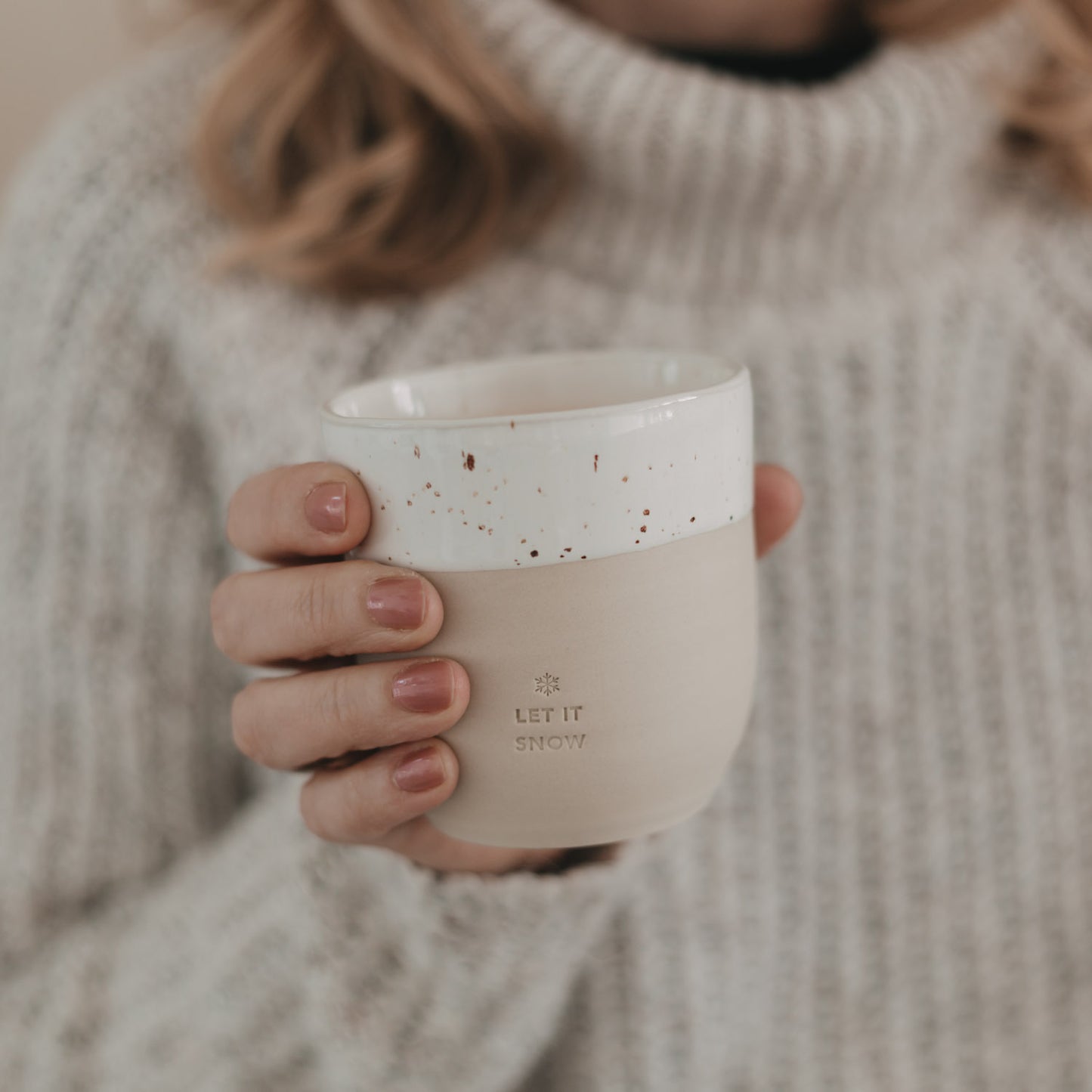 Frau hält Becher „Let it Snow“ mit heißem Getränk in der Hand
