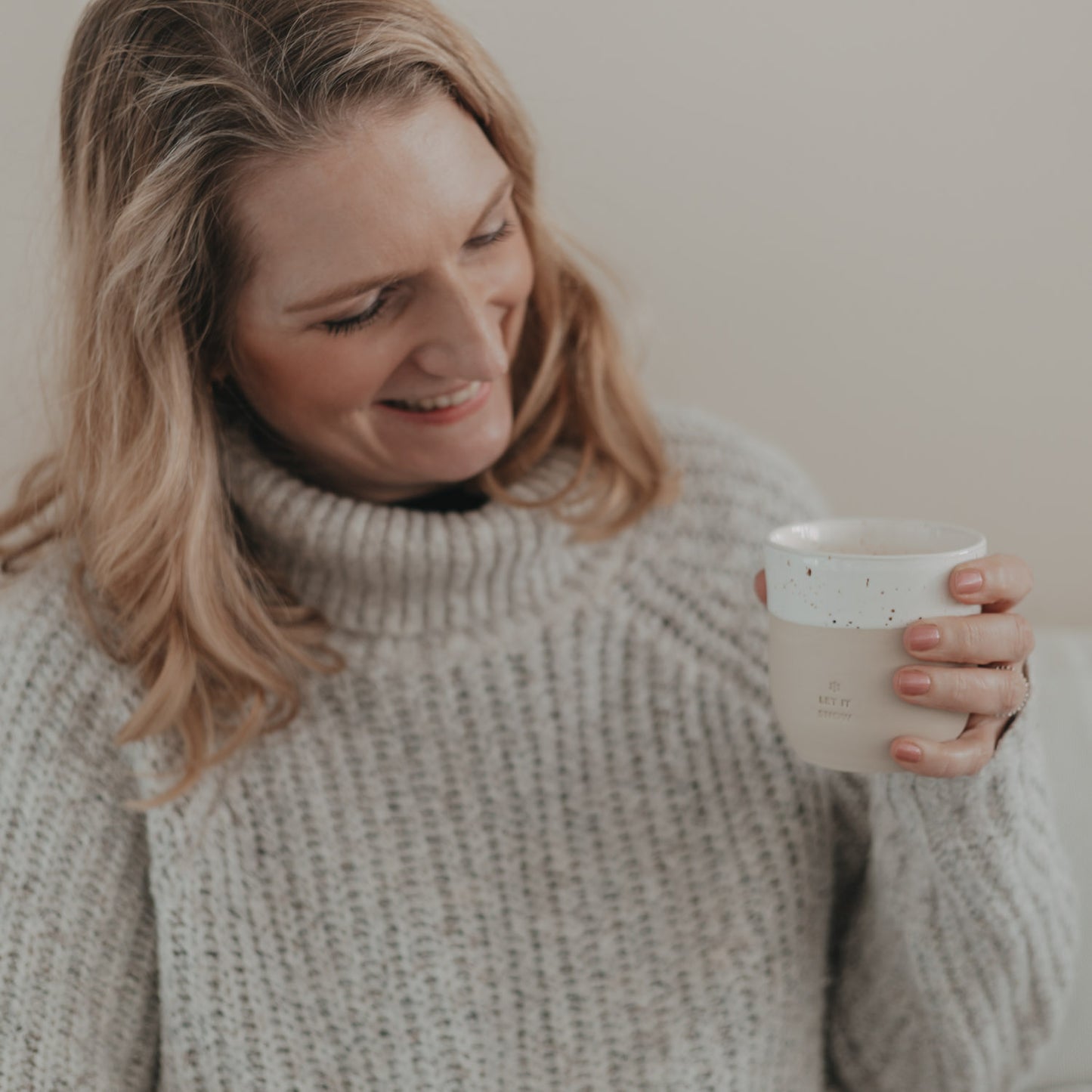 Frau lächelt und hält Becher „Let it Snow“ in gemütlicher Atmosphäre