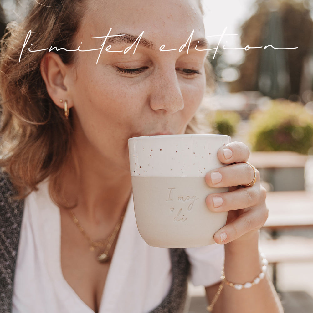 Frau im Dirndl trinkt aus dem Becher „I mog di“ und genießt den Moment in der Sonne.