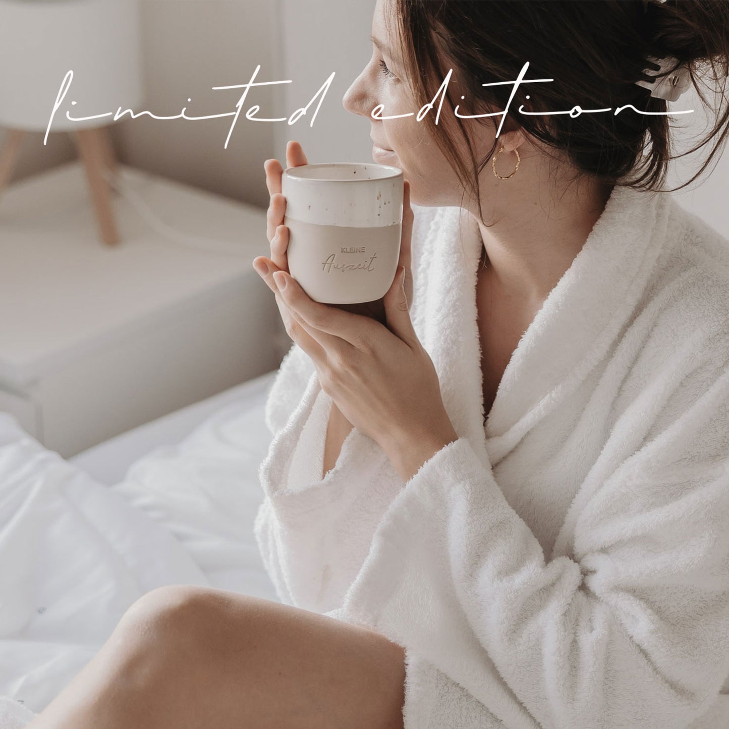 Frau im Bademantel hält Keramikbecher „Kleine Auszeit“ in ruhiger Morgenstimmung – Limited Edition.