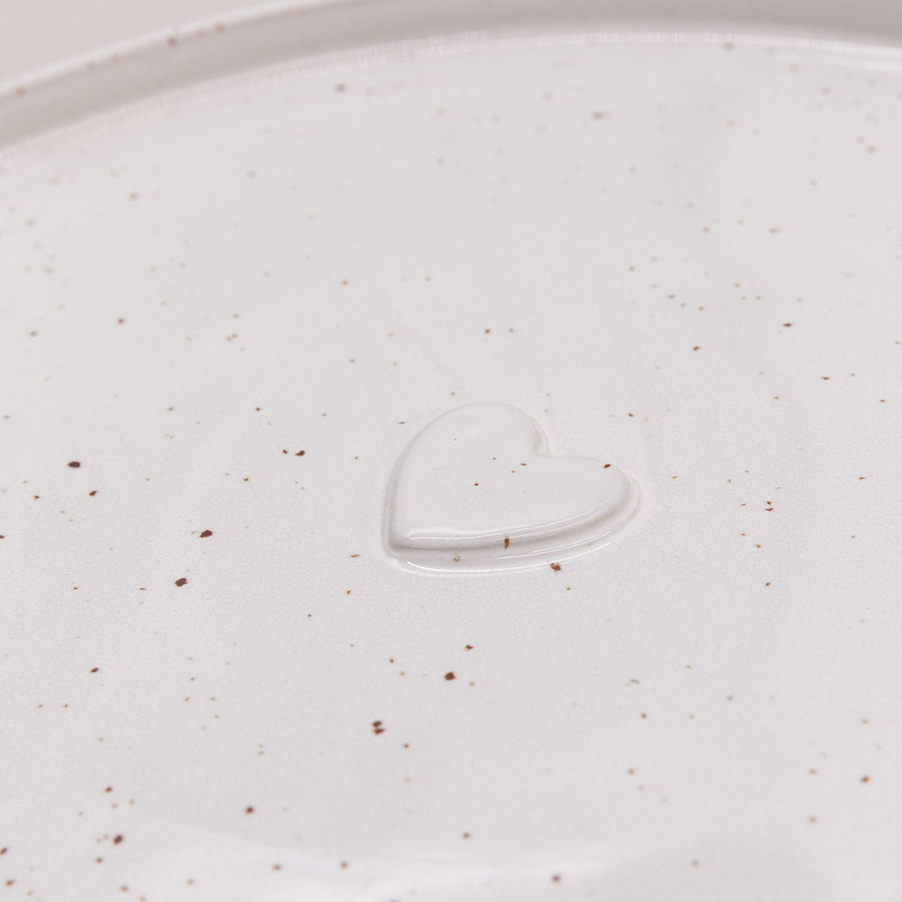 Herzdetail des Calma Speisetellers in Cremeweiß mit feinen Sprenkeln und erhabener Prägung