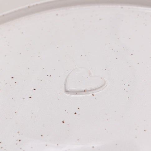 Herzdetail des Calma Speisetellers in Cremeweiß mit feinen Sprenkeln und erhabener Prägung