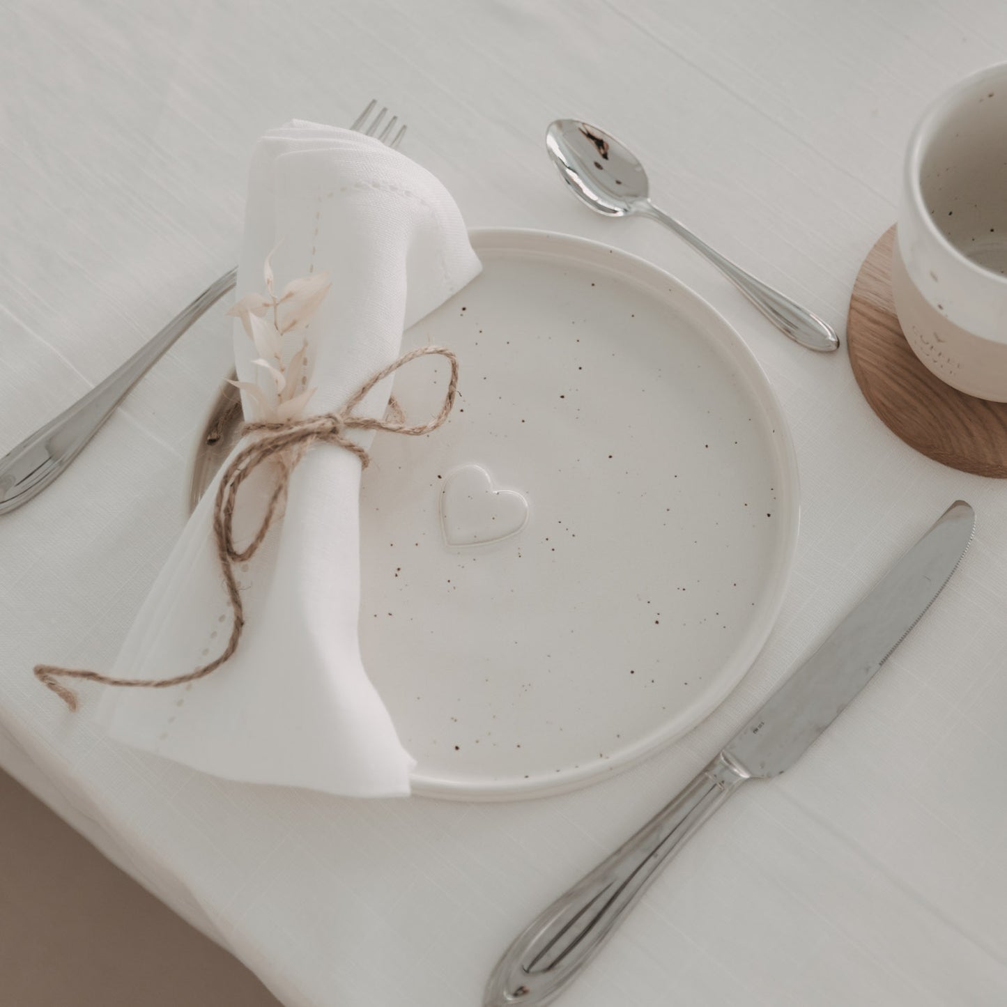 Frühstücksteller Calma aus Keramik mit Herzdetail, liebevoll gedeckt mit Stoffserviette und Besteck auf hellem Tisch.