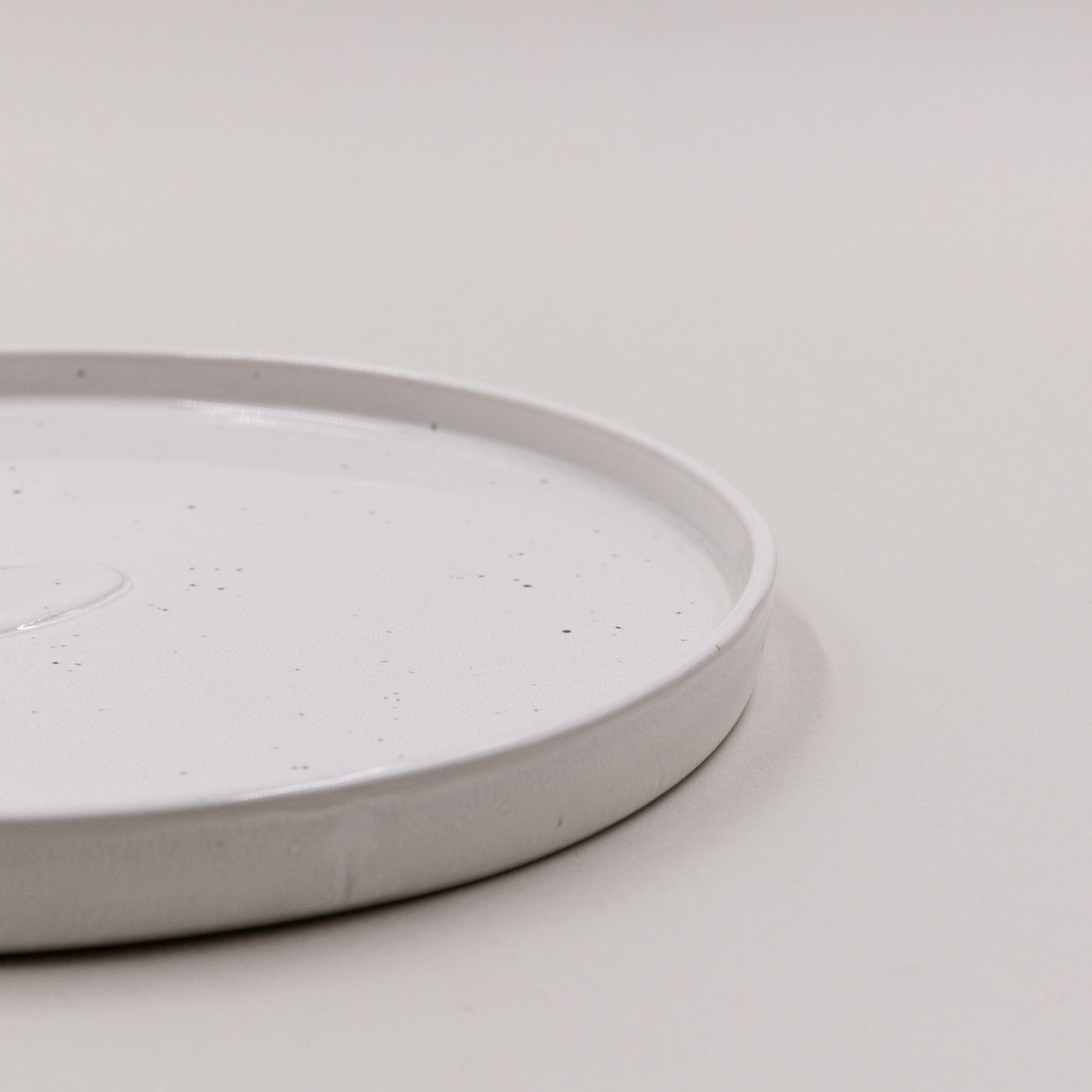 Nahaufnahme der erhöhten Tellerkante des Calma Frühstückstellers mit feinen braunen Sprenkeln.