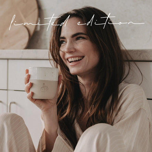 Lächelnde Frau hält Limited Edition Keramikbecher mit geprägter Handgeste in einer hellen Umgebung.