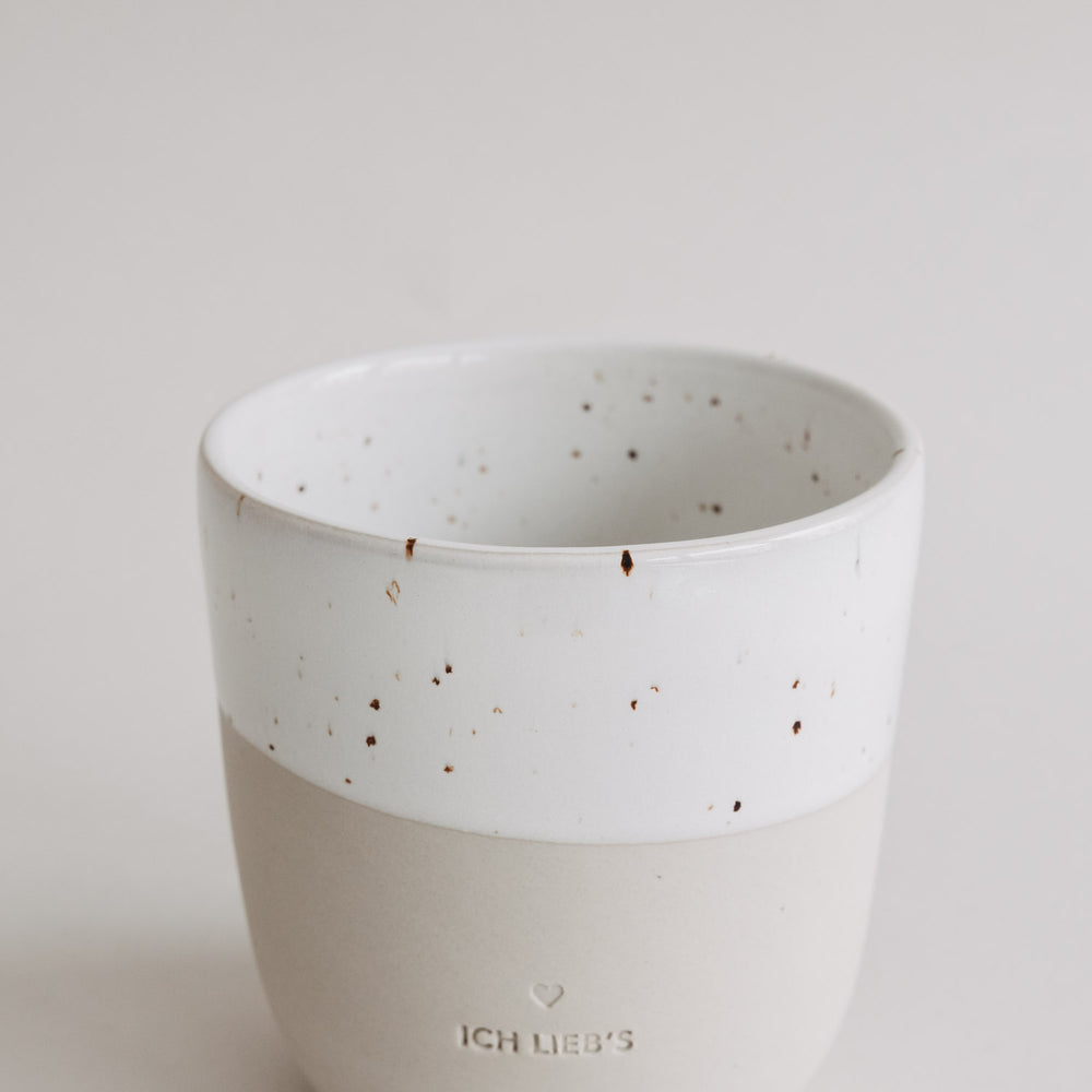 Detailaufnahme der gesprenkelten weißen Glasur der „Ich lieb’s“-Tasse mit beiger Unterseite.