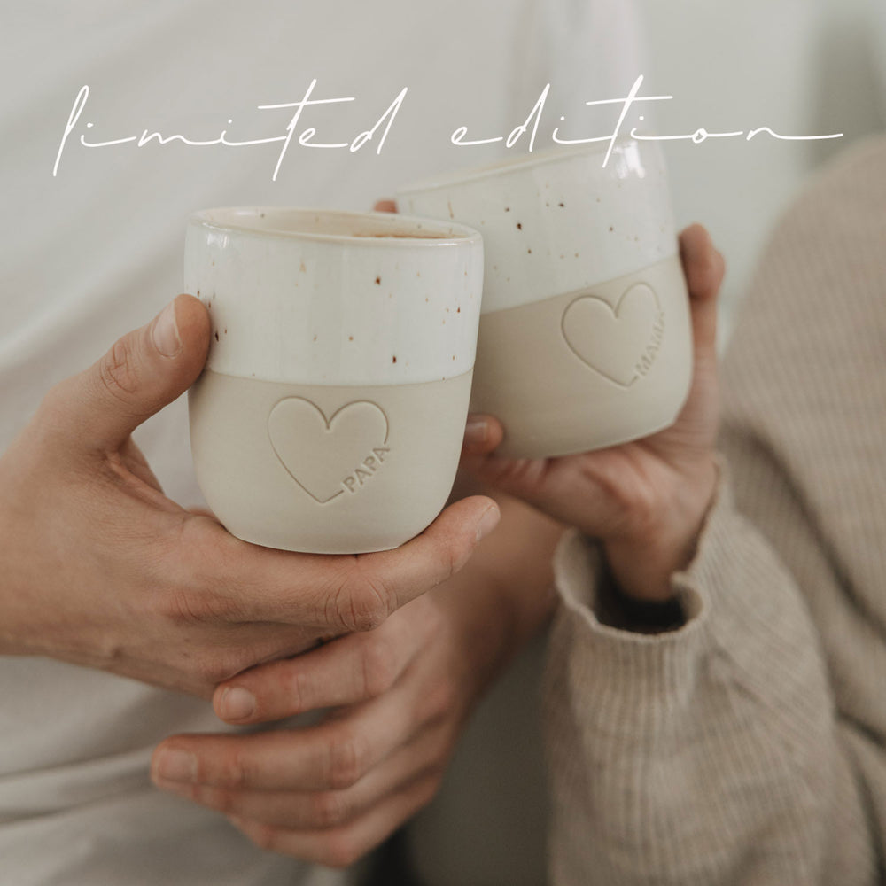 Zwei Keramikbecher Papa und Mama mit Herzmotiv beim Anstoßen, gemütliche Szene, Limited Edition