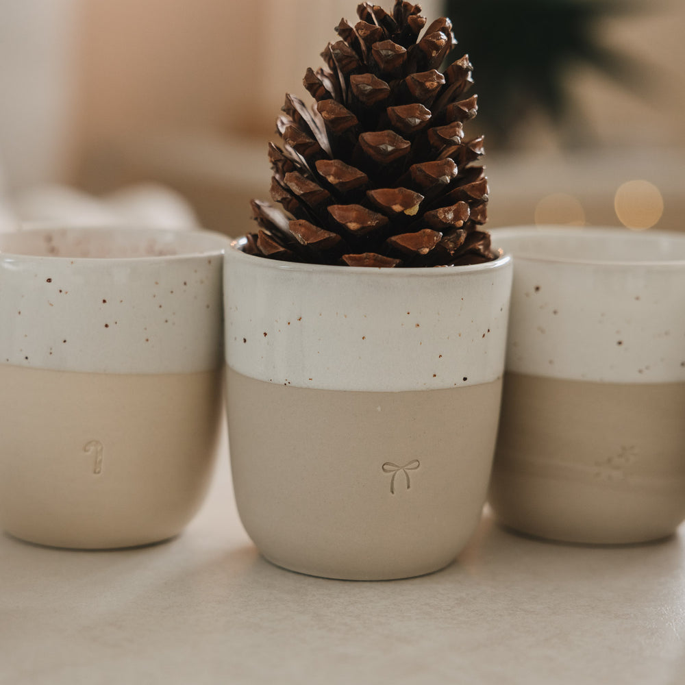 Keramikbecher mit Schleifenprägung und Tannenzapfen, Detailaufnahme stilvoller Winterdekoration