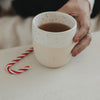 Keramikbecher mit Zuckerstangen-Motiv, gefüllt mit Tee, daneben Zuckerstange, minimalistisch und winterlich