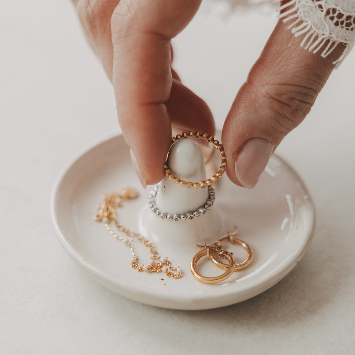 Nahaufnahme einer weißen Schmuckablage aus Keramik mit Ringhalter und Goldschmuck