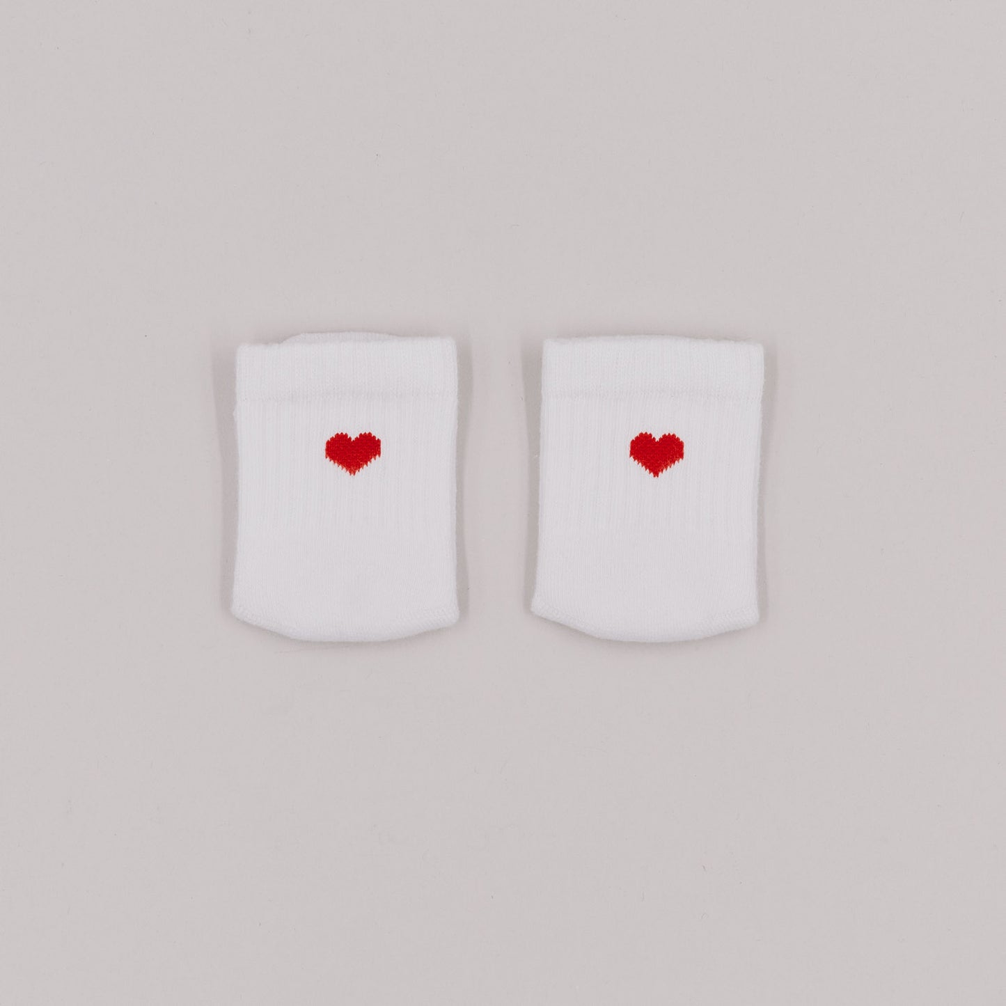 Weiße Babysocken mit gesticktem rotem Herz auf der Vorderseite, liebevoll nebeneinander auf hellgrauem Hintergrund platziert.