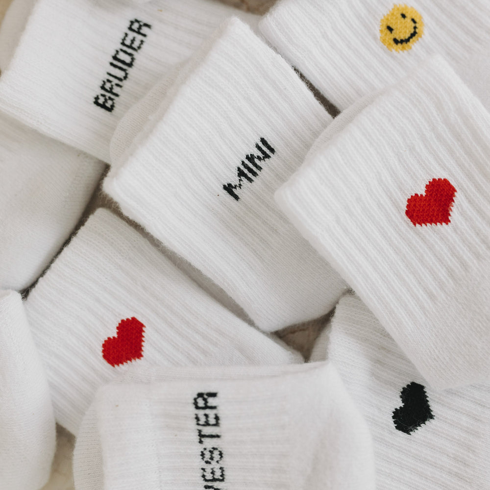 Mix aus verschiedenen Babysocken mit Schriftzug und Symbolen – darunter auch das schwarze Herz-Design.