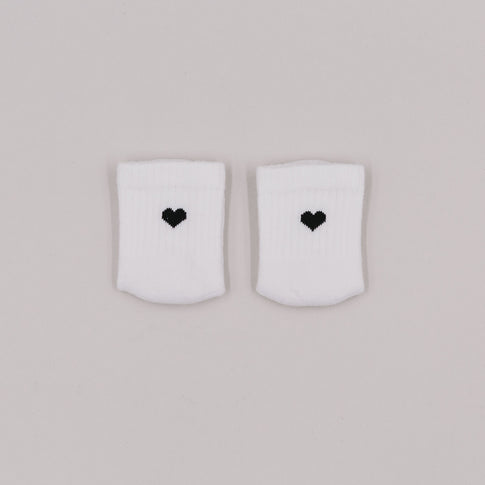Weiße Babysocken mit gesticktem schwarzen Herz auf hellem Hintergrund, liebevoll nebeneinander drapiert.