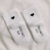 Detailaufnahme von Babysocken mit schwarzem Herz und Eulenschnitt-Schriftzug auf der Fußsohle.