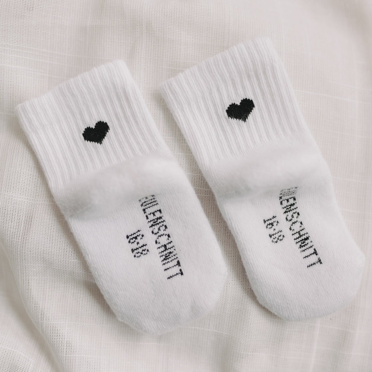 Detailaufnahme von Babysocken mit schwarzem Herz und Eulenschnitt-Schriftzug auf der Fußsohle.