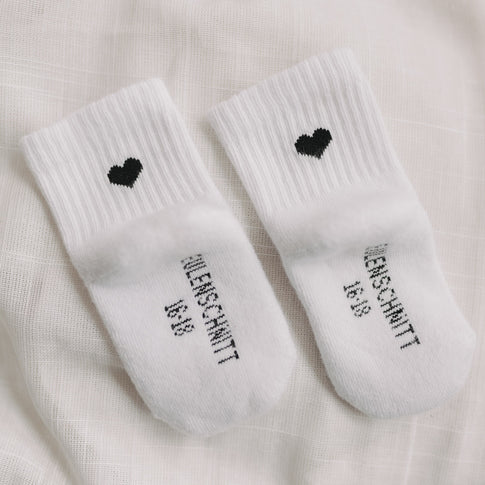 Detailaufnahme von Babysocken mit schwarzem Herz und Eulenschnitt-Schriftzug auf der Fußsohle.