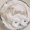 Zwei Babysocken mit schwarzem Herz auf weißem Stoff, dekorativ mit Holzschriftzug „Mama“ arrangiert.