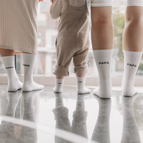 Familienfoto mit Socken: Mama, Papa und Kind tragen passende weiße Socken mit Mama-, Papa- und Mini-Schriftzug.