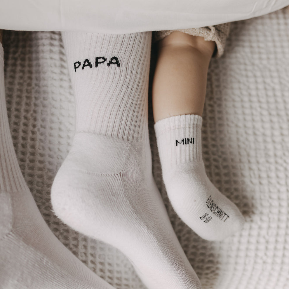 Kuschelige Familienmomente mit Papa- und Mini-Socken auf weichem Bett.