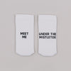 Weiße Socken mit der Aufschrift „Meet me“ und „Under the mistletoe“ auf grauem Hintergrund nebeneinander liegend
