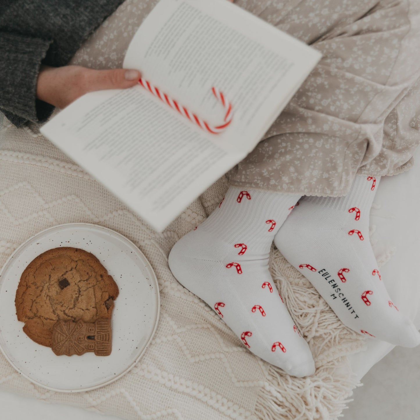 Person liest ein Buch mit Zuckerstangen-Socken an den Füßen – gemütliche Winterstimmung.
