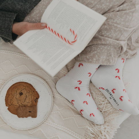 Person liest ein Buch mit Zuckerstangen-Socken an den Füßen – gemütliche Winterstimmung.