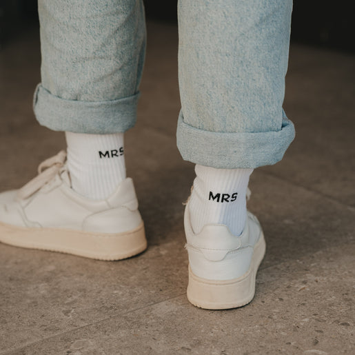 Detailansicht weißer Socken „MRS“ mit Sneakern und hochgekrempelter Jeans