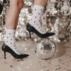 Weiße Socken mit schwarzen Herzen und schwarze High Heels in einer festlichen Szene mit großer Discokugel, silbernem Konfetti und glitzerndem Hintergrund.