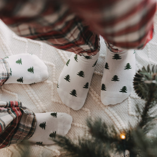 Weiße Eulenschnitt Socken mit grünen Tannen für Erwachsene und Kinder in weihnachtlicher Atmosphäre.