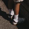 Weiße Kindersocken mit roten Herzen von Eulenschnitt, getragen zu hellen Sneakern.