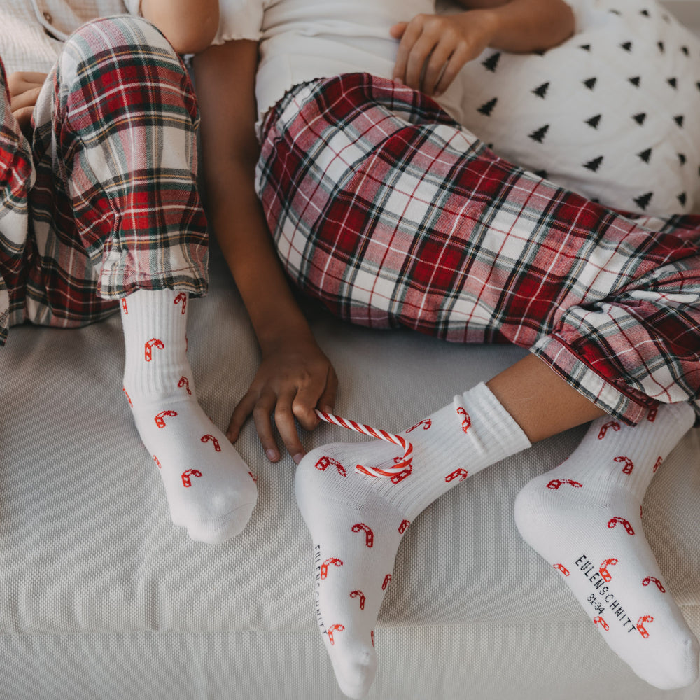 Kinder tragen weiße Eulenschnitt Socken mit roten Zuckerstangen zu Weihnachten