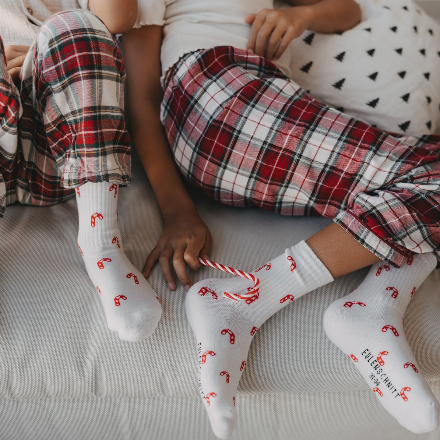 Kinder tragen weiße Eulenschnitt Socken mit roten Zuckerstangen zu Weihnachten