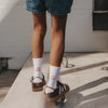 Kind trägt weiße Kids Socken Der Boden ist Lava mit roter Schrift und braunen Sneakern beim Balancieren.