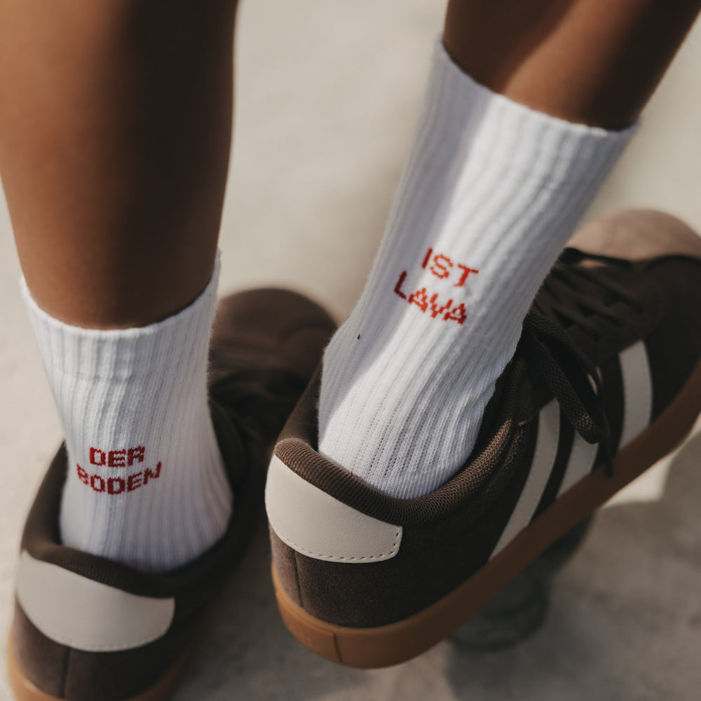 Weiße Kids Socken Der Boden ist Lava mit roter Stickerei in braunen Sneakern.