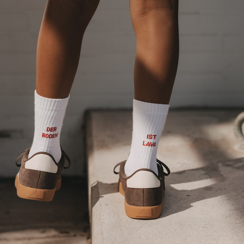 Kind in weißen Socken Der Boden ist Lava mit rotem Schriftzug beim Balancieren auf einer Kante.