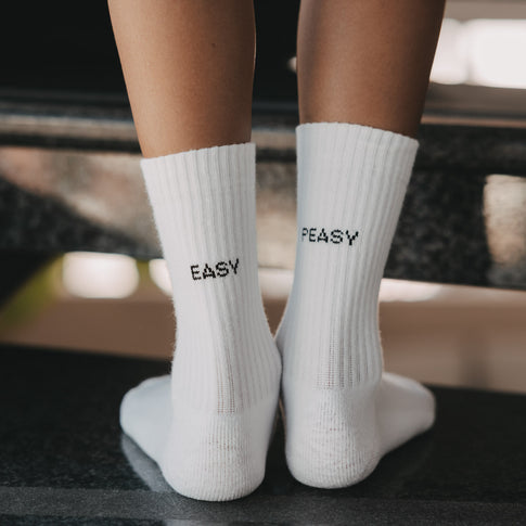Nahaufnahme der weißen Kindersocken mit den schwarzen Schriftzügen „Easy“ und „Peasy“.