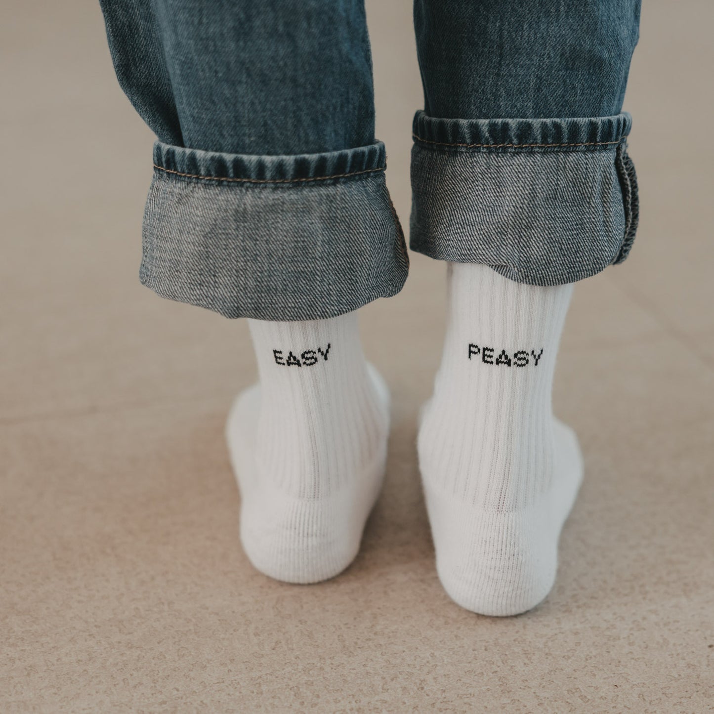 Weiße Kindersocken mit schwarzem Easy Peasy Schriftzug und umgeschlagener Jeans.