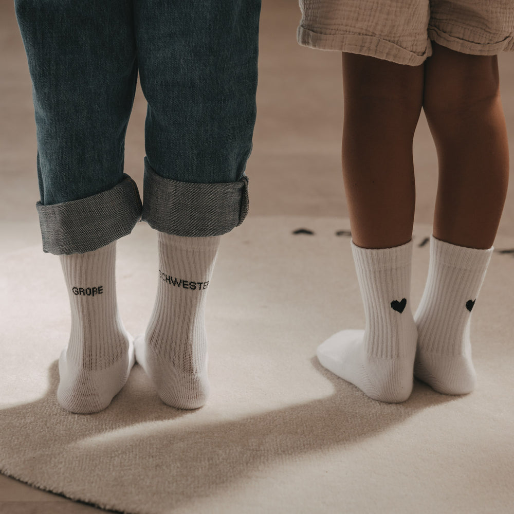 Weiße Kids Socken Große Schwester mit schwarzem Schriftzug neben Kindersocken mit schwarzen Herzen